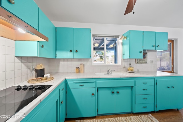 kitchen with ventilation hood, blue cabinets, sink, tasteful backsplash, and black cooktop