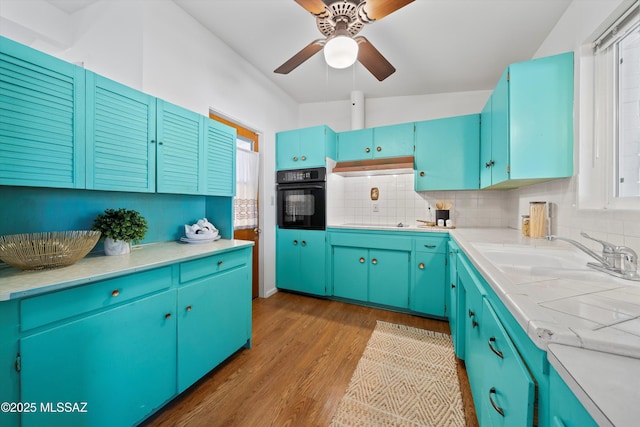 kitchen with decorative backsplash, sink, blue cabinetry, black oven, and lofted ceiling