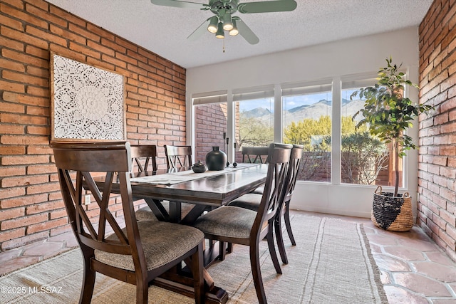 dining room with brick wall, ceiling fan, a mountain view, and a textured ceiling