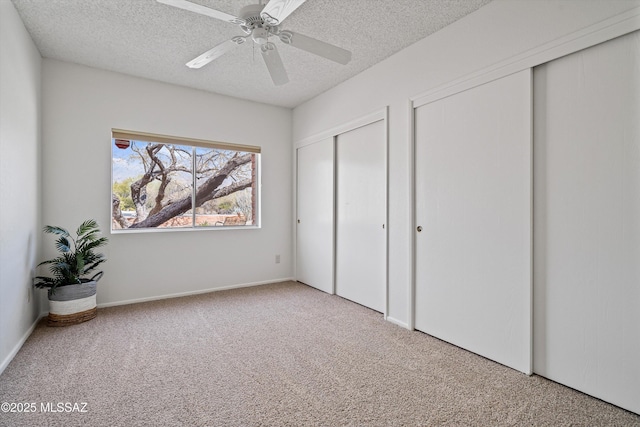 unfurnished bedroom with carpet, two closets, a textured ceiling, and ceiling fan