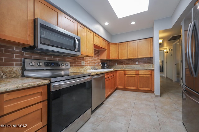 kitchen featuring a skylight, sink, light tile patterned floors, light stone counters, and stainless steel appliances