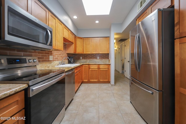 kitchen featuring sink, light tile patterned floors, appliances with stainless steel finishes, backsplash, and a skylight