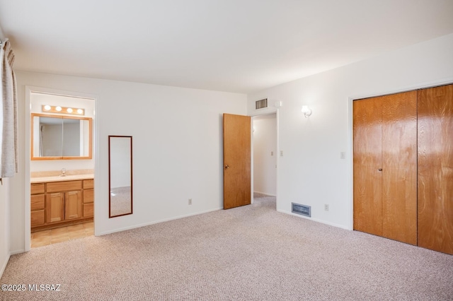 unfurnished bedroom featuring sink, light colored carpet, ensuite bath, and a closet