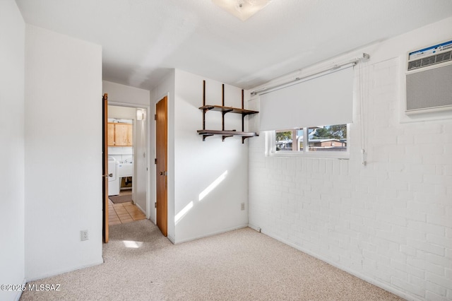 carpeted spare room featuring brick wall, washer / clothes dryer, and a wall mounted AC