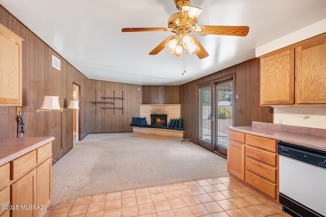 kitchen featuring wooden walls, a fireplace, ceiling fan, white dishwasher, and light carpet