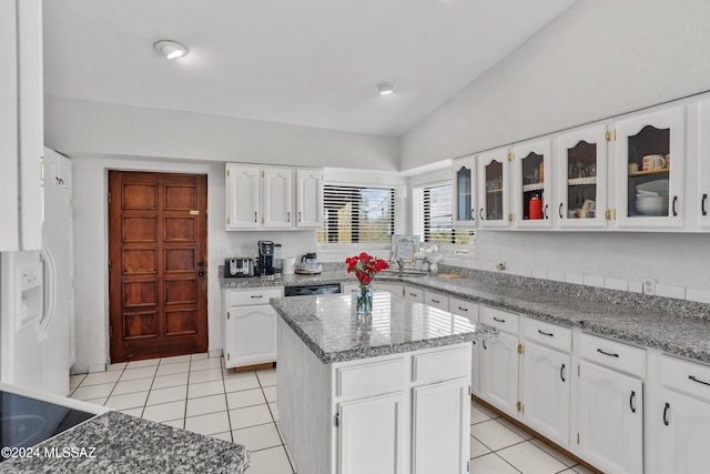 kitchen with white cabinets, a kitchen island, light stone countertops, and lofted ceiling