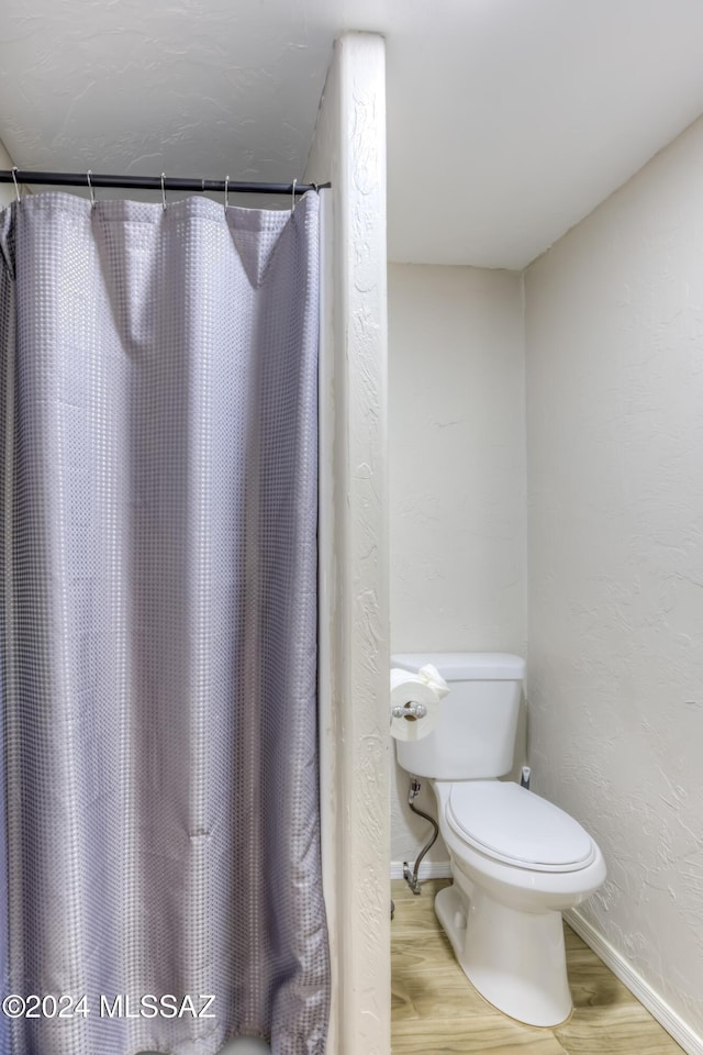 bathroom with hardwood / wood-style floors, toilet, and a shower with curtain