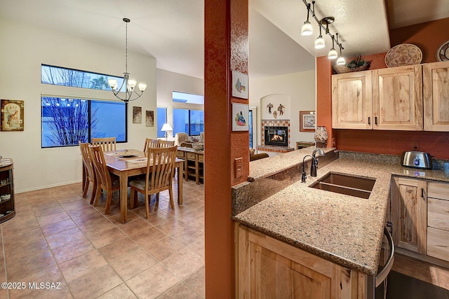 kitchen featuring light stone counters, sink, light brown cabinets, pendant lighting, and a tiled fireplace