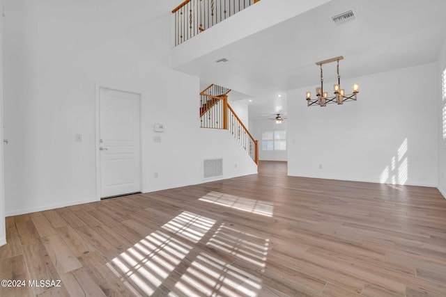 unfurnished living room with ceiling fan with notable chandelier, light wood-type flooring, and a high ceiling