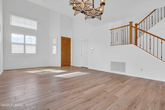 unfurnished living room with light hardwood / wood-style floors, a high ceiling, and an inviting chandelier