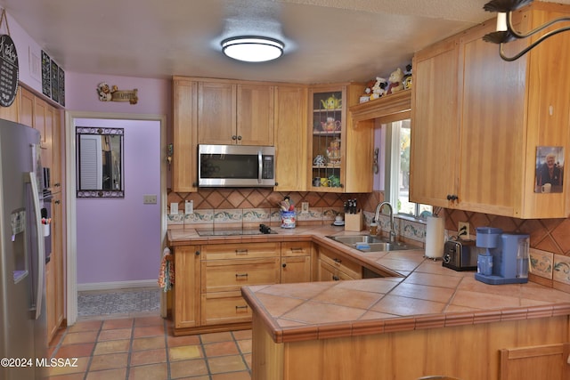 kitchen with decorative backsplash, appliances with stainless steel finishes, kitchen peninsula, sink, and tile countertops