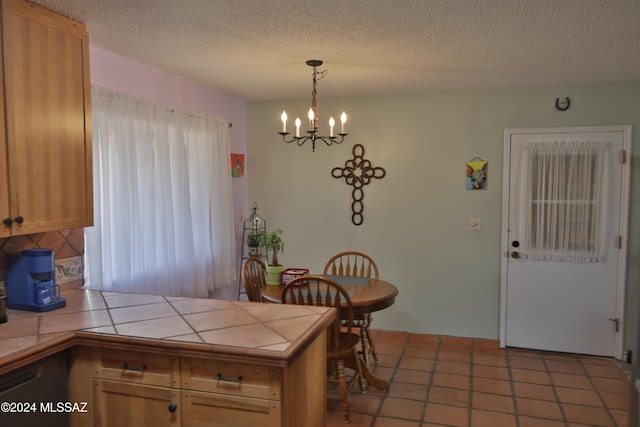 kitchen with a textured ceiling, plenty of natural light, tile counters, and a notable chandelier