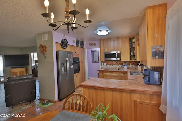 kitchen featuring tasteful backsplash, stainless steel appliances, sink, a chandelier, and tile counters