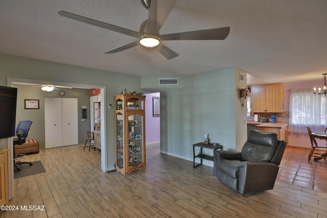 living room with a textured ceiling, ceiling fan with notable chandelier, and light hardwood / wood-style flooring