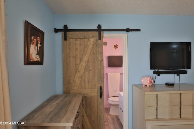 bedroom with a barn door, ensuite bath, light hardwood / wood-style floors, and a textured ceiling