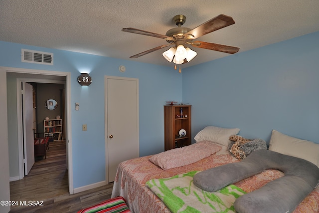 bedroom with a textured ceiling, ceiling fan, and dark wood-type flooring