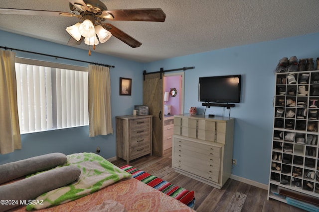 bedroom featuring ceiling fan, a barn door, dark hardwood / wood-style flooring, and a textured ceiling