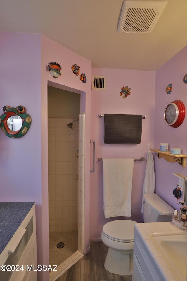 bathroom featuring hardwood / wood-style floors, vanity, toilet, and tiled shower