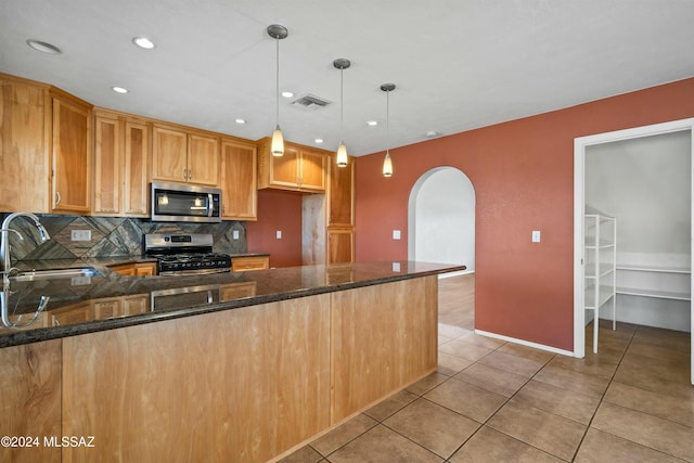 kitchen featuring appliances with stainless steel finishes, sink, hanging light fixtures, and dark stone countertops