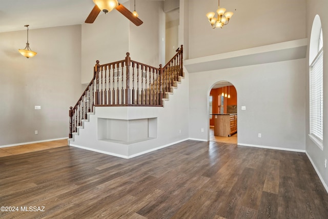 unfurnished living room with dark wood-type flooring, ceiling fan with notable chandelier, and a towering ceiling