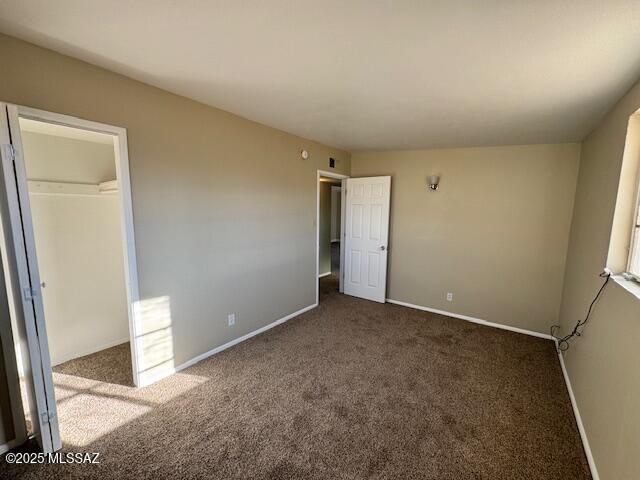 unfurnished bedroom featuring a spacious closet, a closet, and dark carpet