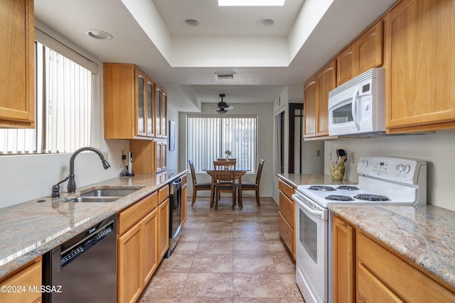 kitchen featuring ceiling fan, sink, a raised ceiling, light stone counters, and white appliances