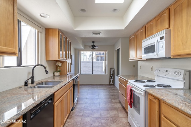 kitchen with white appliances, glass insert cabinets, light stone countertops, a tray ceiling, and a sink