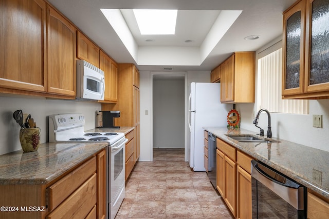 kitchen featuring a skylight, a tray ceiling, stone countertops, a sink, and white appliances