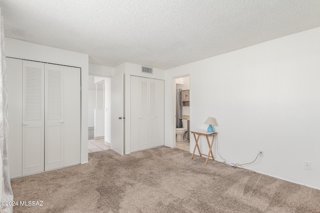 unfurnished bedroom with a textured ceiling, light colored carpet, and ensuite bath