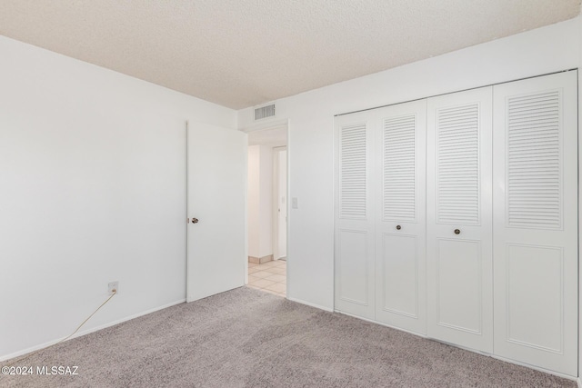 unfurnished bedroom with a textured ceiling, light carpet, and a closet