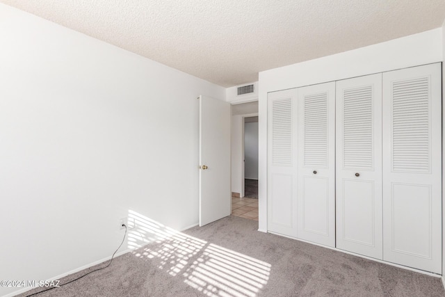 unfurnished bedroom featuring a textured ceiling, light carpet, and a closet