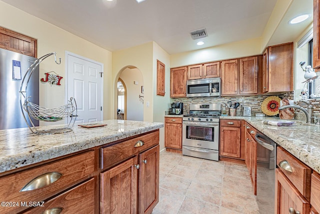 kitchen featuring appliances with stainless steel finishes, backsplash, and light stone counters