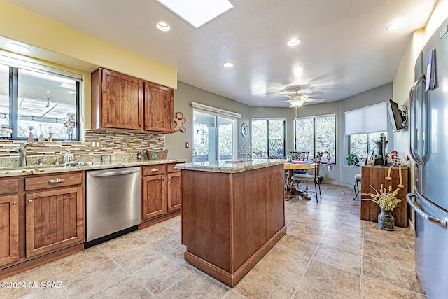 kitchen featuring appliances with stainless steel finishes, tasteful backsplash, light stone counters, ceiling fan, and a center island