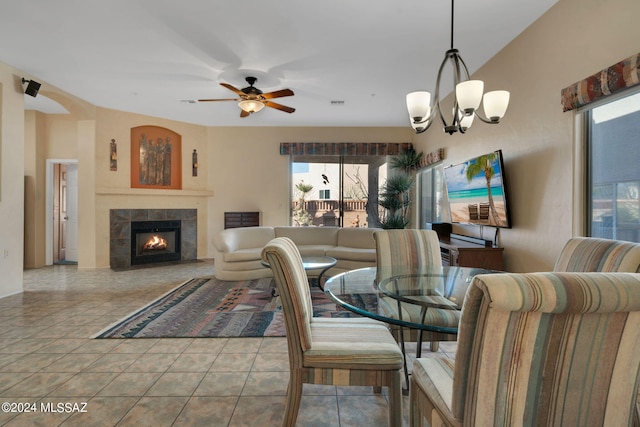 tiled dining area featuring ceiling fan with notable chandelier and a tiled fireplace