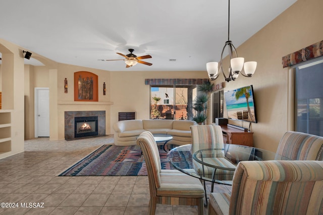 dining room featuring a tiled fireplace, light tile patterned flooring, and ceiling fan with notable chandelier