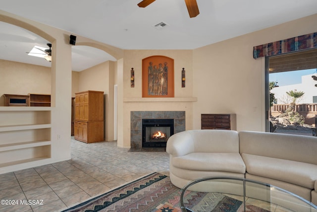 living room with built in shelves, ceiling fan, and a tiled fireplace