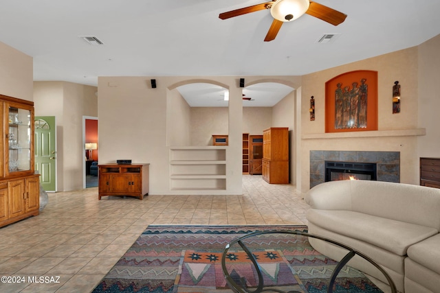 living room with a fireplace, built in features, ceiling fan, and light tile patterned flooring