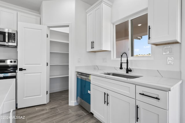 kitchen with white cabinetry, sink, light stone counters, light hardwood / wood-style flooring, and appliances with stainless steel finishes