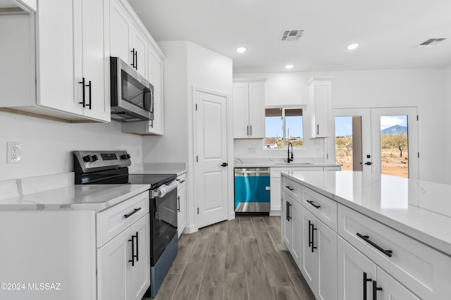 kitchen with white cabinetry, sink, light stone counters, light hardwood / wood-style floors, and appliances with stainless steel finishes