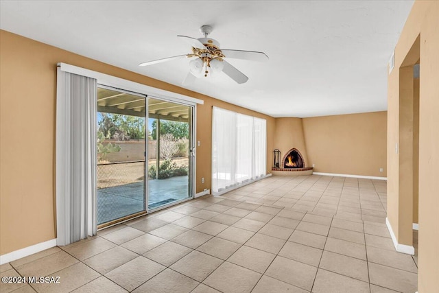 unfurnished living room featuring ceiling fan, a large fireplace, and light tile patterned floors