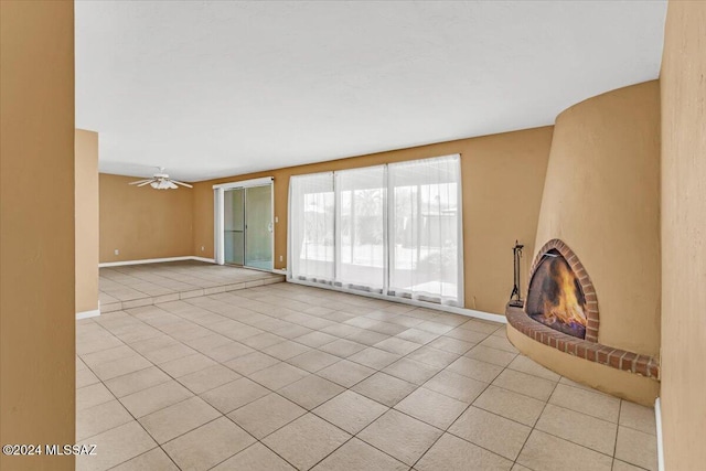 unfurnished living room with a brick fireplace, ceiling fan, and light tile patterned flooring