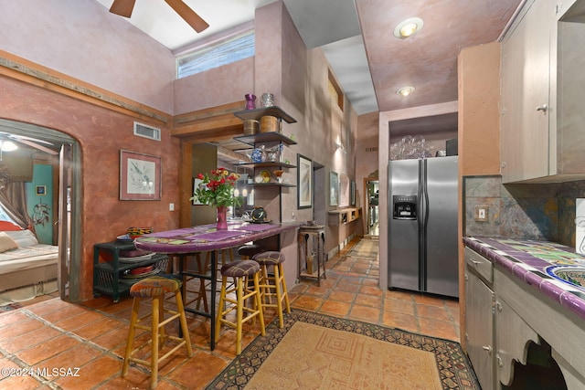 kitchen featuring stainless steel fridge with ice dispenser, a towering ceiling, tile countertops, and ceiling fan