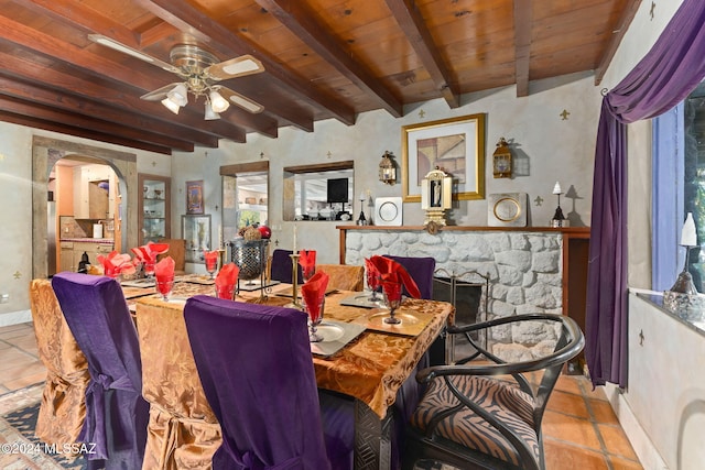 tiled dining room with beam ceiling, a stone fireplace, and wooden ceiling