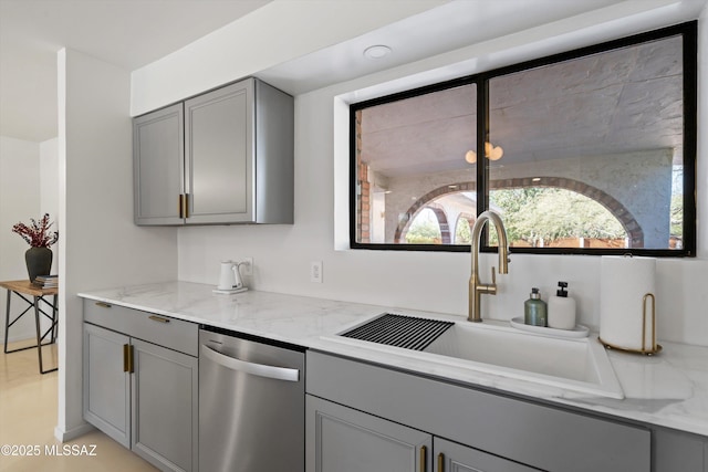 kitchen with gray cabinetry, sink, stainless steel dishwasher, and light stone countertops