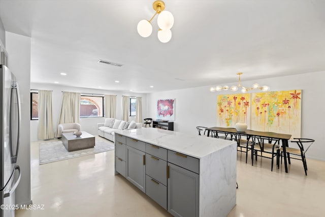 kitchen featuring light stone counters, hanging light fixtures, stainless steel fridge, gray cabinets, and a notable chandelier