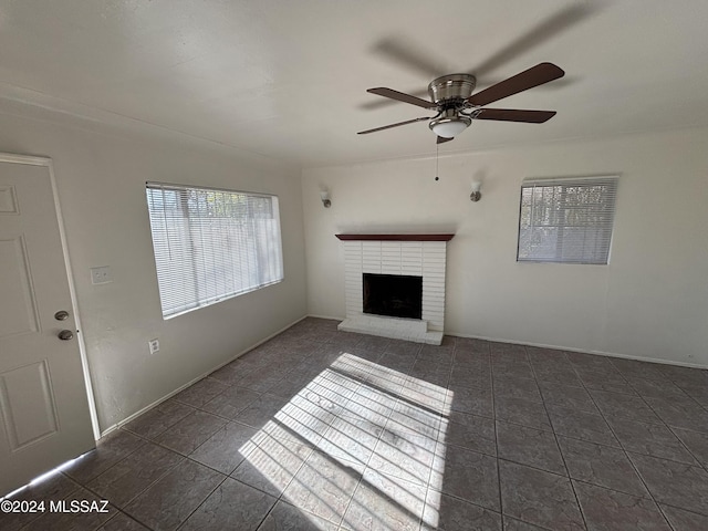 unfurnished living room with ceiling fan, dark tile patterned flooring, and a brick fireplace