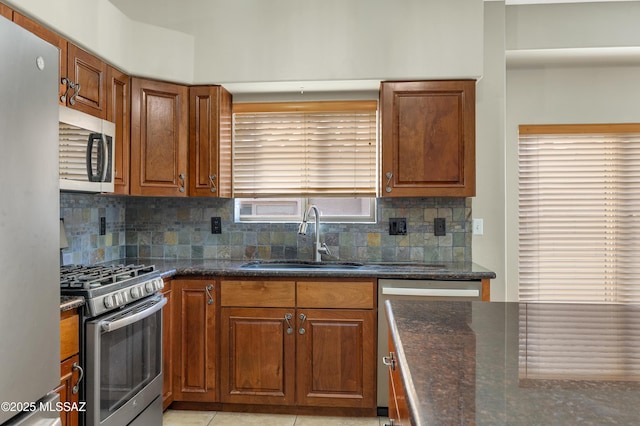 kitchen featuring sink, light tile patterned floors, dark stone countertops, stainless steel appliances, and decorative backsplash