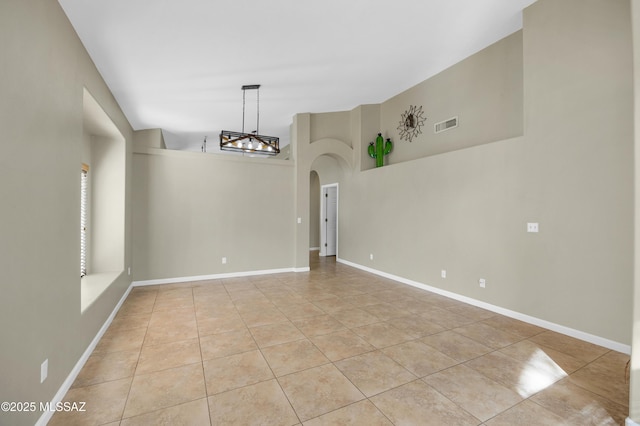 tiled spare room featuring a towering ceiling and an inviting chandelier