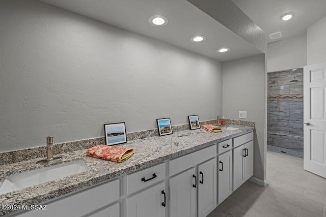 bathroom with tile patterned flooring, a tile shower, and vanity