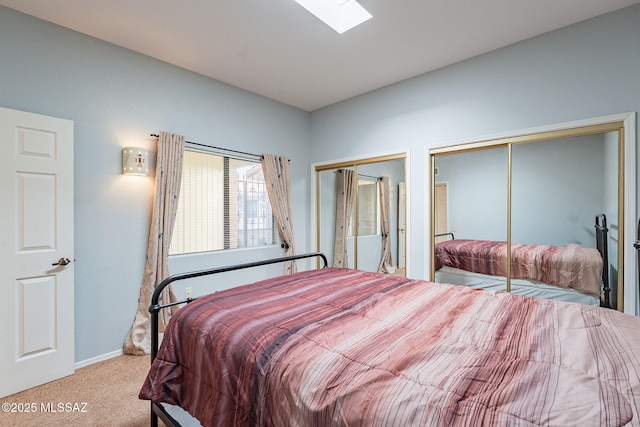 bedroom featuring two closets, light colored carpet, and a skylight